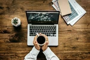 Image of a person holding coffee by a computer for Real Wealth Show Podcast Episode #650
